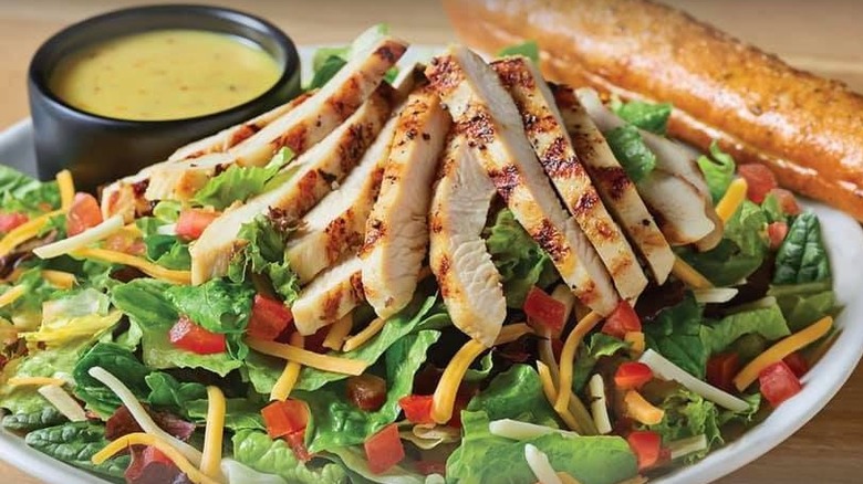 fresh Tuscan chicken salad on a white plate with dressing on the side in a black plastic cup at Applebee's