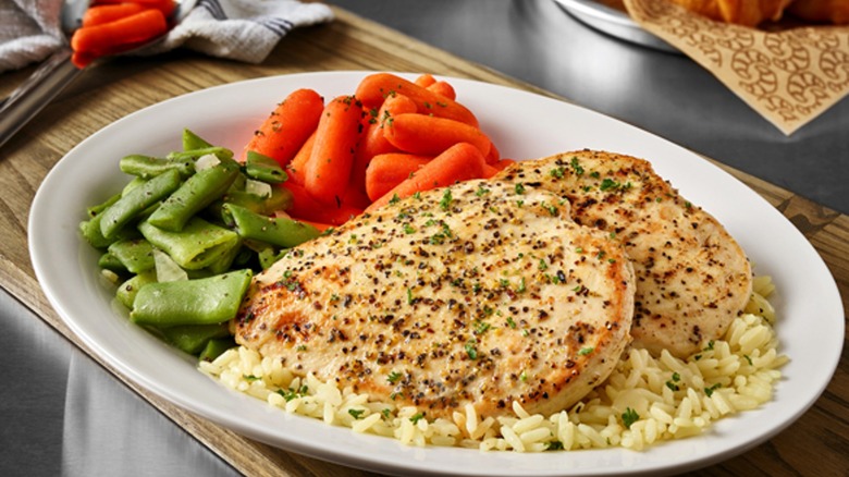 Lemon pepper chicken is served with rice, carrots, and green beans.