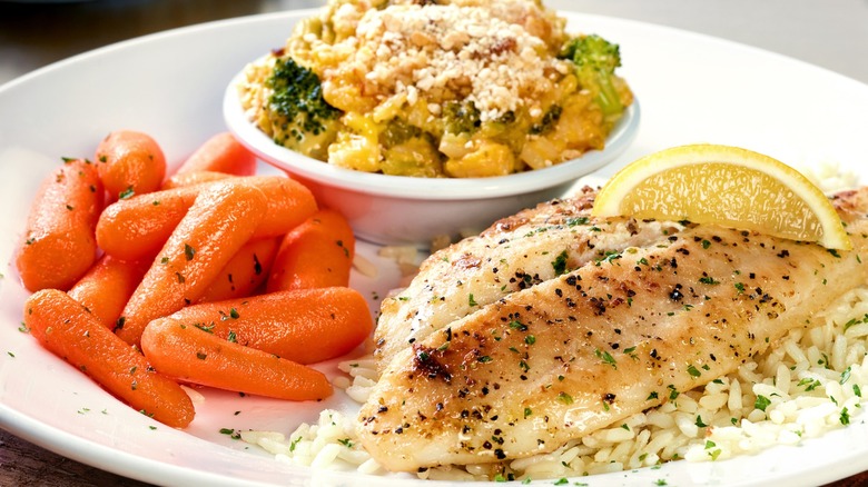 Grilled white fish with lemon over white rice has a side of carrots and broccoli casserole.