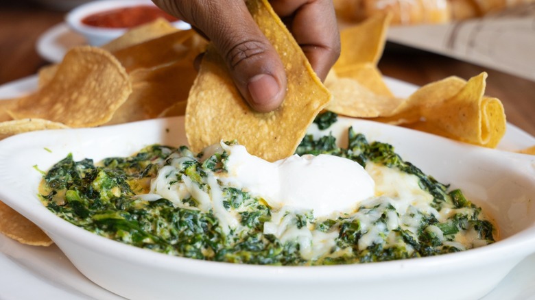 A person dips a tortilla chip into a dish filled with Santa Fe Spinach Dip.