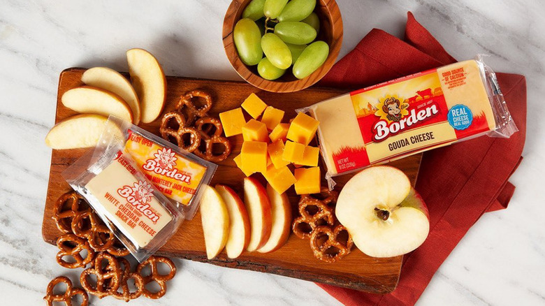 A snack board with borden cheese, apples, grapes, and pretzels