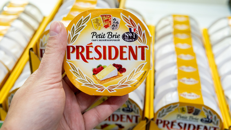 A hand holding a round of president brie