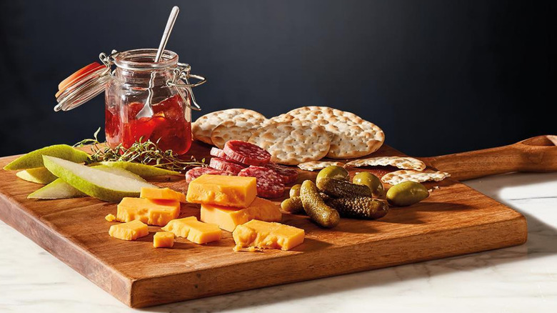 A cheese board with apples, pickles, olives, crackers, meat, and jam