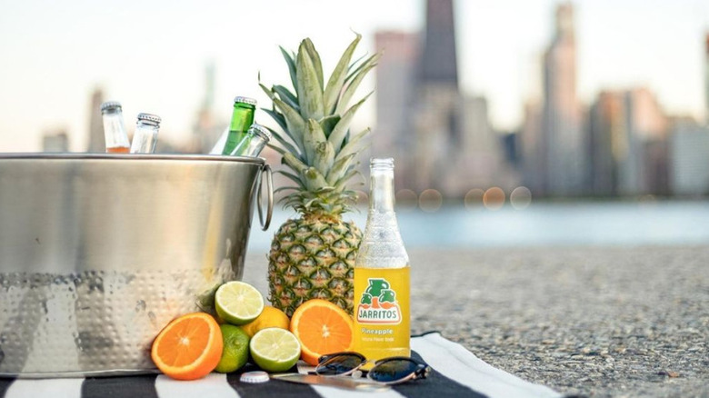 A bottle of pineapple jarritos next to cut citrus in front of a skyline