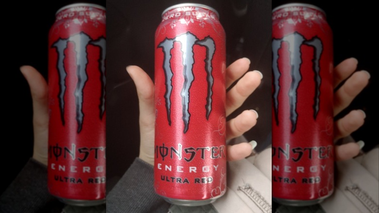 A hand holding Monster Ultra Red can