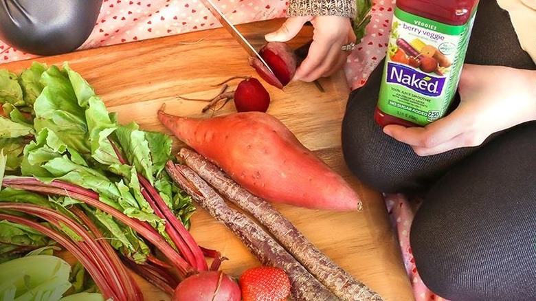 Vegetables on a cutting board at a picnic, and hands holding a bottle of berry veggie juice