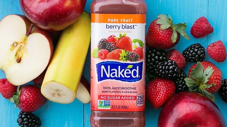 A bottle of Naked Berry blast laying on a light blue surface surrounded by fruits and berries