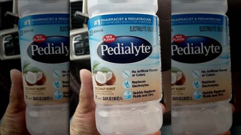 Someone holding bottle of Coconut Burst Pedialyte Classic in car