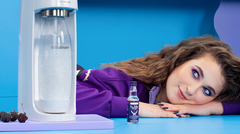 A Woman Dressed in Purple Laying beside a SodaStream and BlackBerryBubly Drops