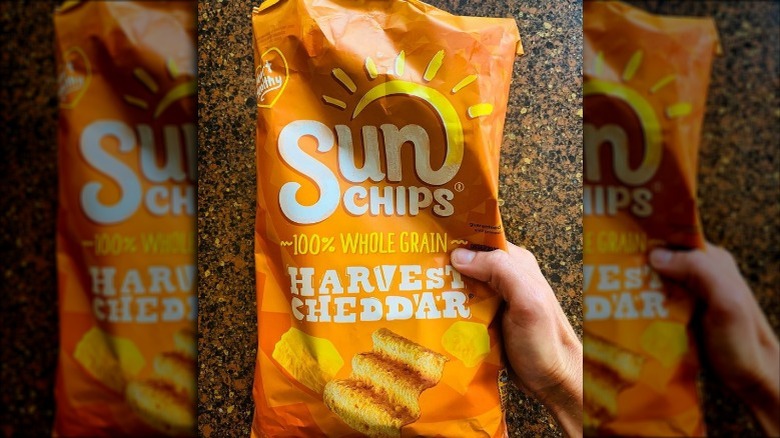 A hand holding a bag of harvest cheddar sun chips