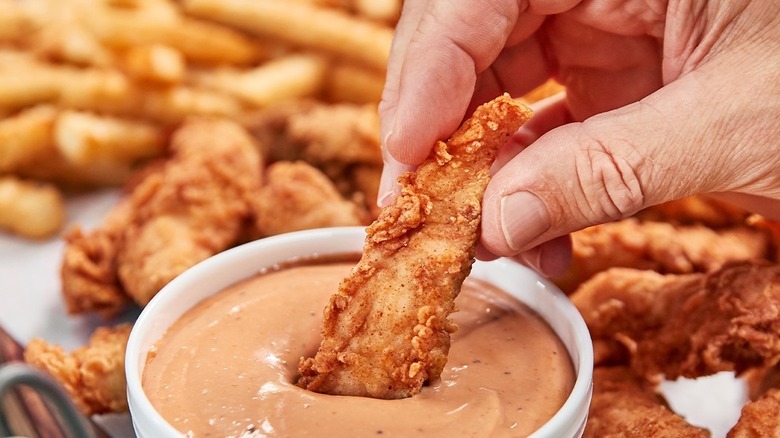 A hand dipping a chicken finger