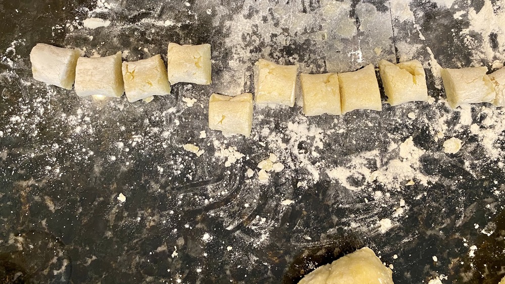 gnocchi dough cut into individual pieces on floured stone counter