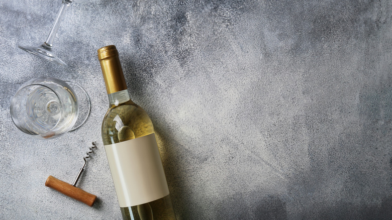 White wine bottle laying down with standing glass and corkscrew on gray background