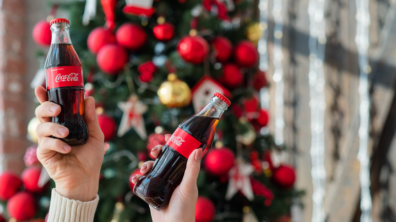 hands holding Coke bottles in front of Christmas tree 