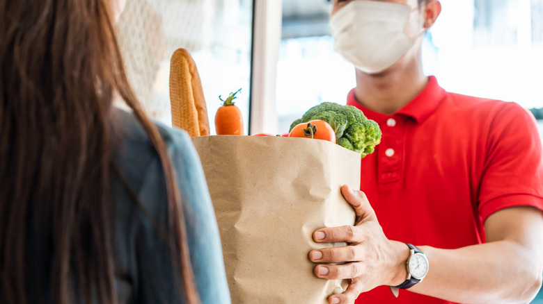 A masked employee handing groceries to a shopper