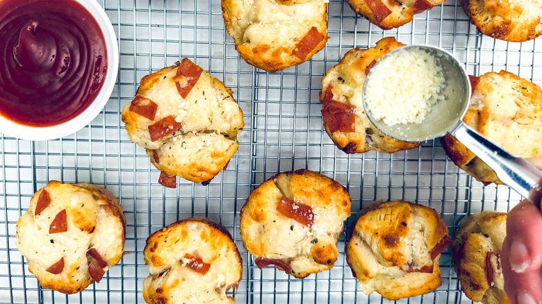 hand sprinkling Parmesan cheese on muffins