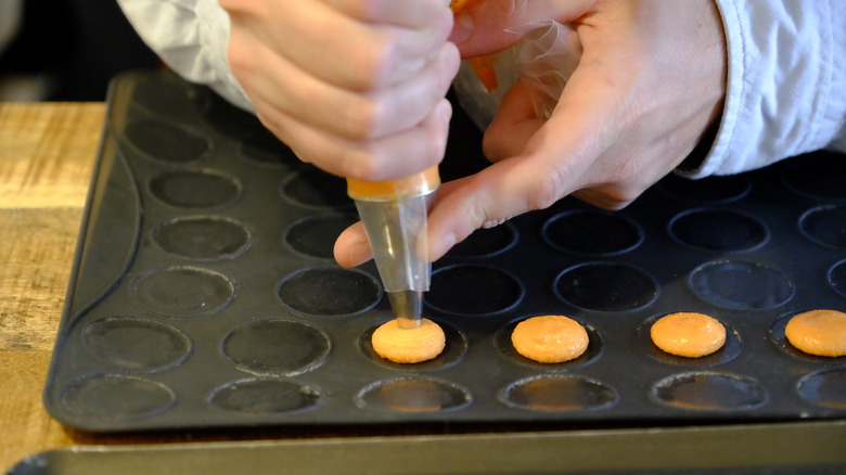 piping macarons on cookie sheet