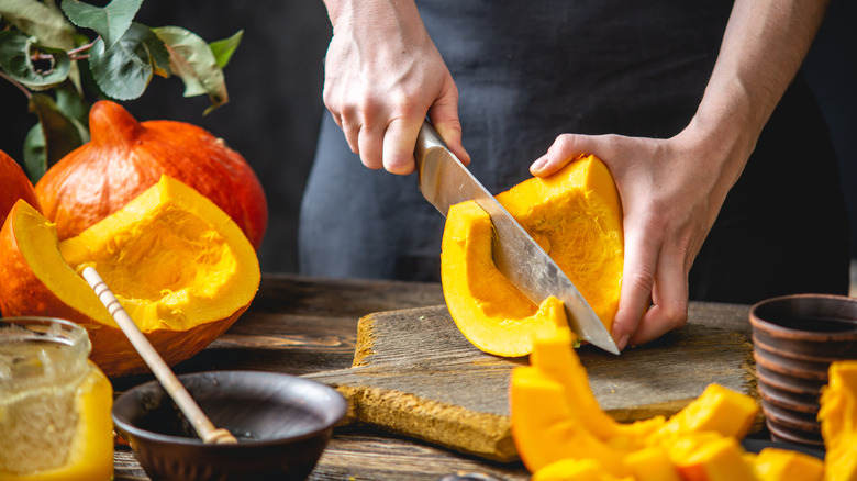 A hand slicing into a pumpkin