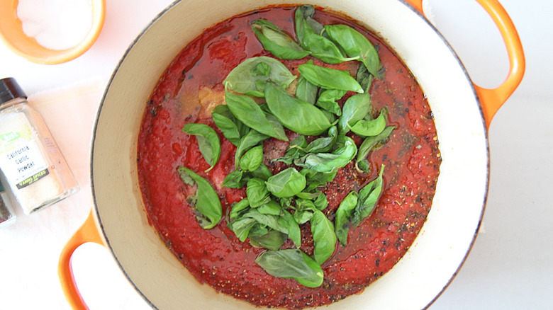 marinara sauce in white enamel cooking pot with fresh basil on top