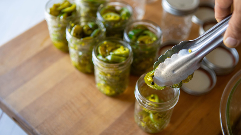 tongs putting jalapeños into jar