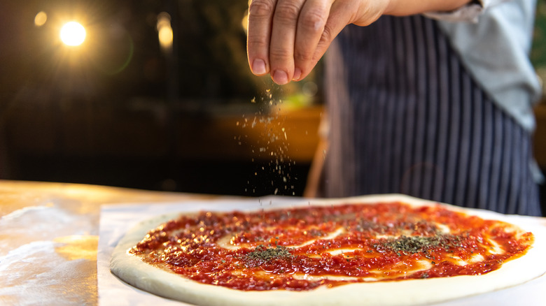 Hand sprinkling seasoning onto pizza