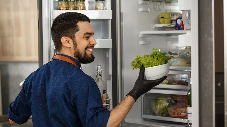 Chef with fridge door open holding salad