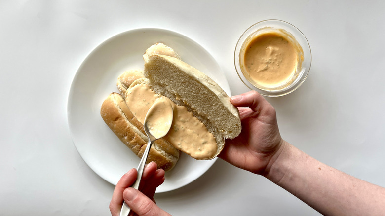 hand spreading mayonnaise on bun