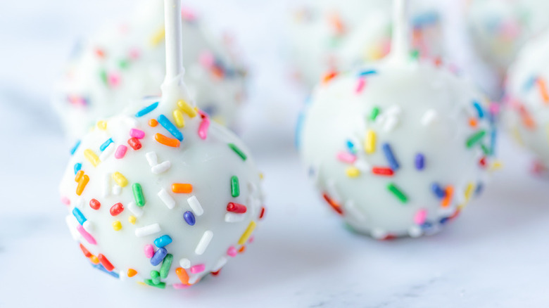 a close-up of cakepops coated in white chocolate and decorate with rainbow sprinkles
