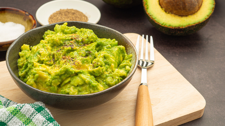 A bowl of guacamole on a chopping board