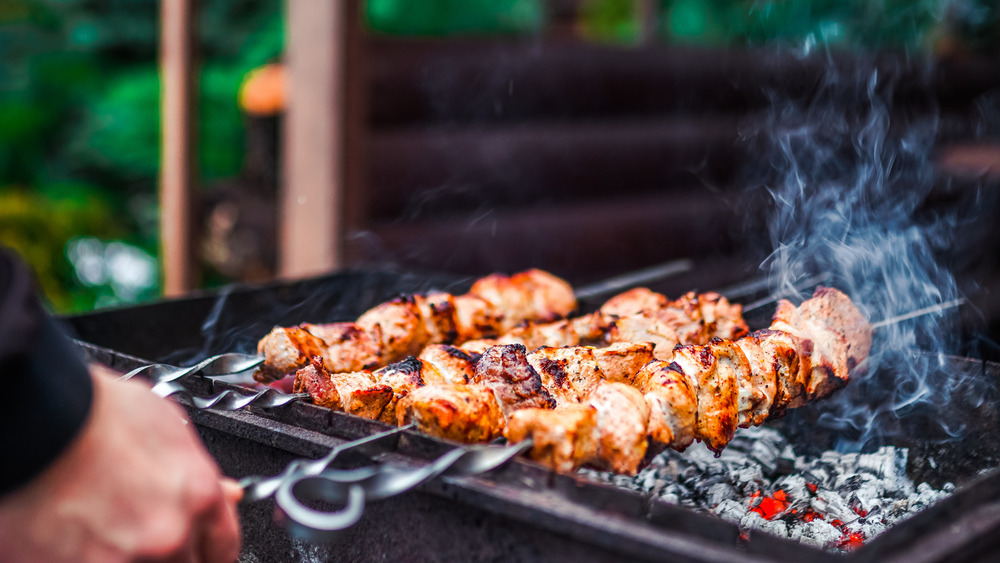 Person grilling kebabs on charcoal