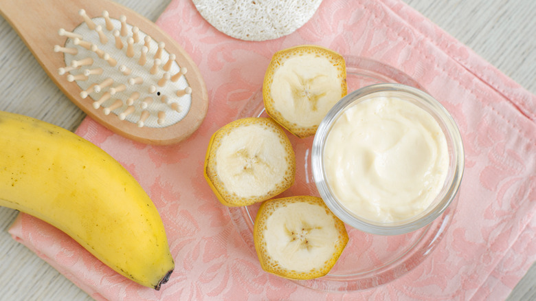 Homemade banana face mask in a glass bowl, next to a wooden brush on a pink towel