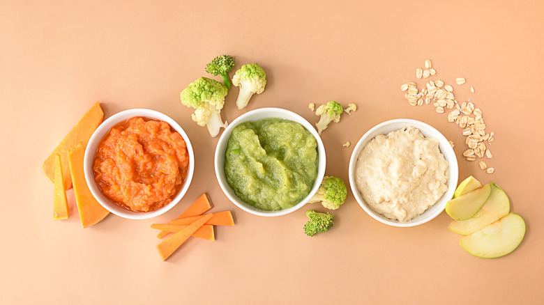 Various baby foods in bowls on peach backdrop