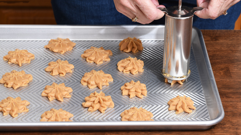 Cookies being squeezed through a cookie press on a baking tray