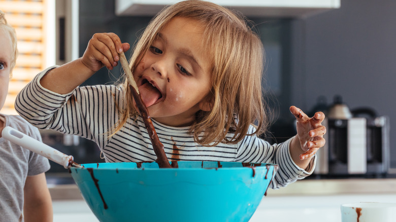 A child eating raw cake batter from the mixing bowl