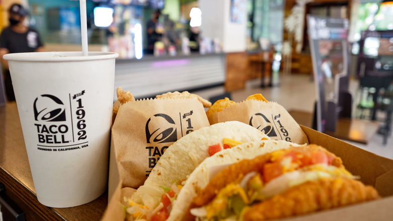  Box set of tasty taco, nachos, and cup of drink served in retail background of taco bell restaurant.