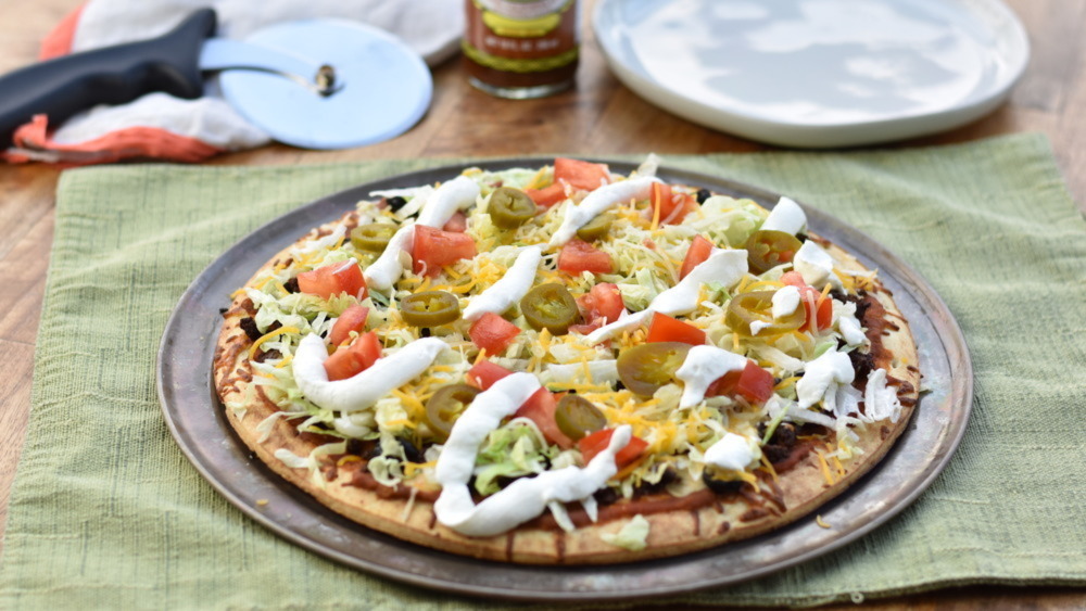 A small pizza on a pan covered in taco toppings.