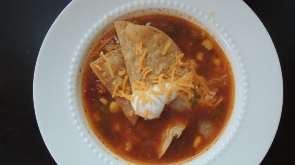 A bowl of tortilla soup topped with chips and sour cream.