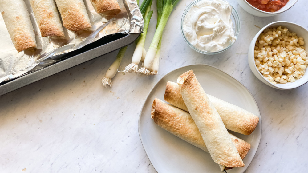 Baked taquitos next to fresh ingredients.