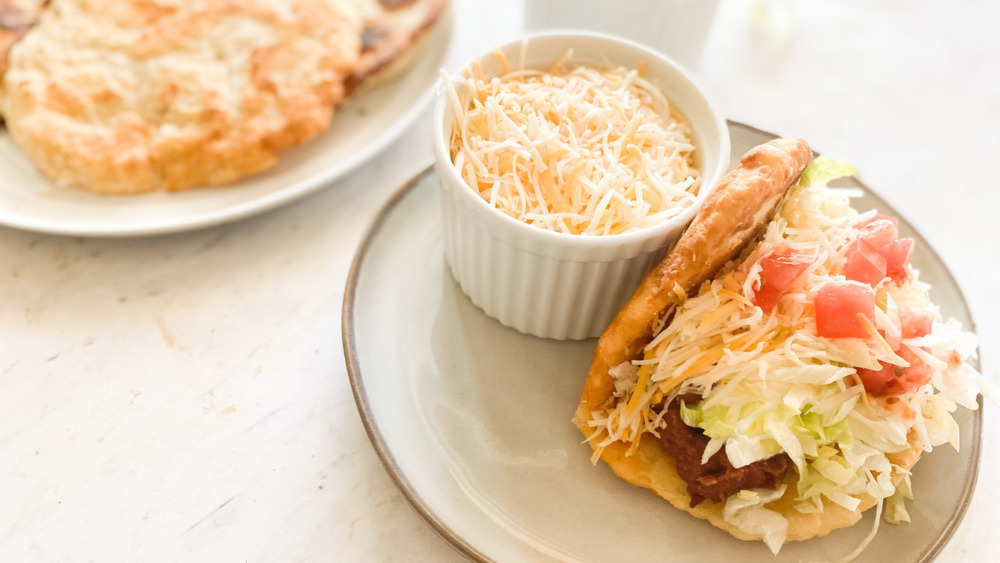 A taco made with a chalupa, next to a bowl of shredded cheese.