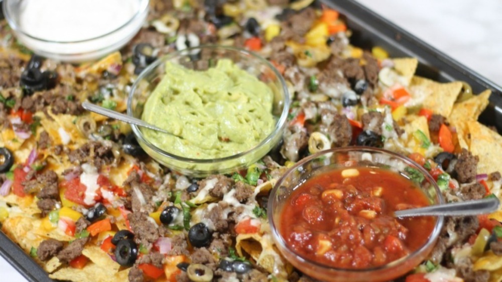 A baking sheet covered in nachos and three dipping sauces.