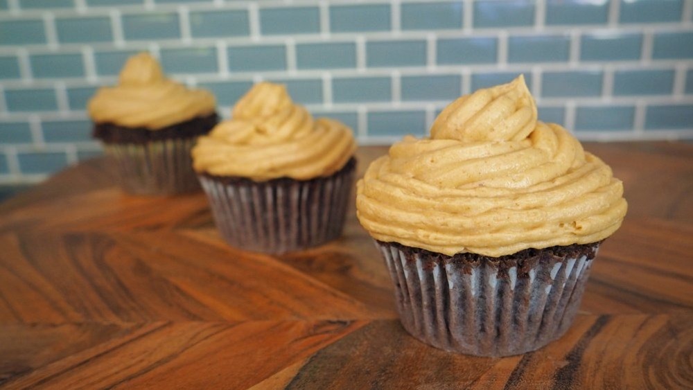 peanut butter frosting atop three chocolate cupcakes on a wooden table