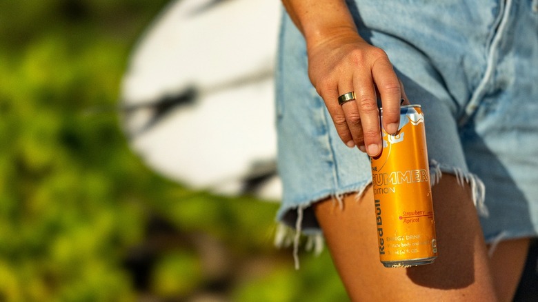 woman in denim shorts holding Red Bull apricot can