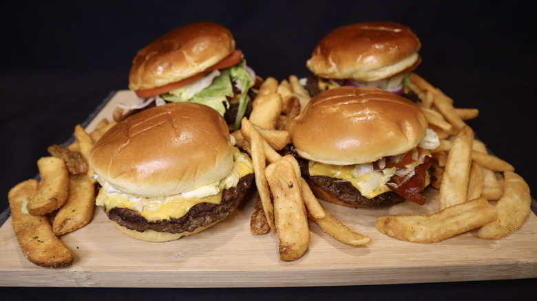 Four burgers on wooden cutting board