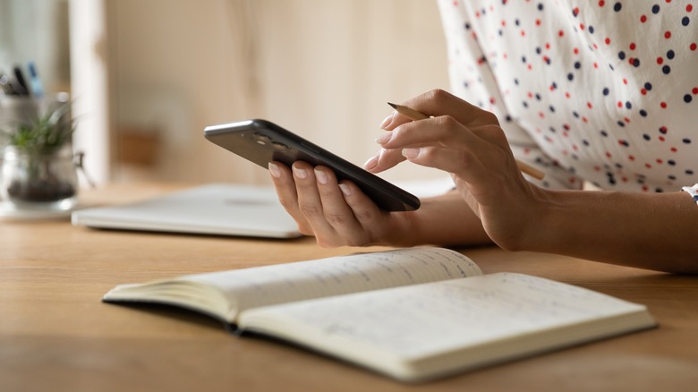 Person sitting at desk with open notebook and phone in hand