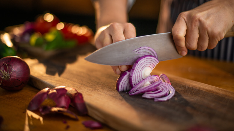 A person cutting red onions on a chopping board