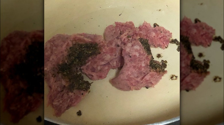 Ground pork in pan with clumps of aggregated seasoning 