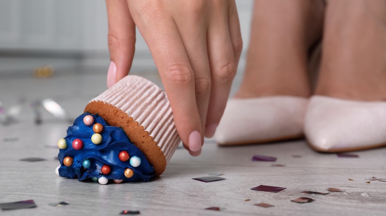 person picking cupcake up off floor