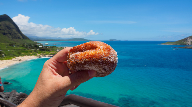 Hand holding malasada with ocean background