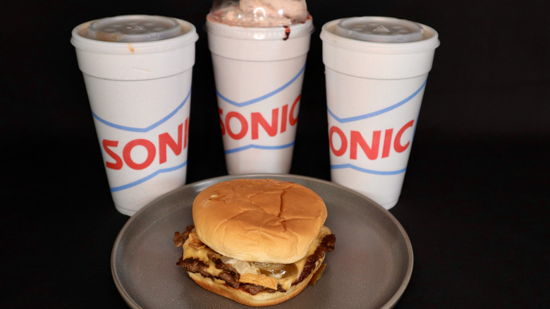 burger on plate with three Sonic cups behind