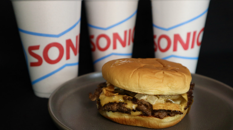 burger on plate with three Sonic cups behind